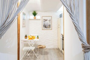 A narrow hallway with a white brick wall, a small table with yellow items, a plant, and a framed picture.