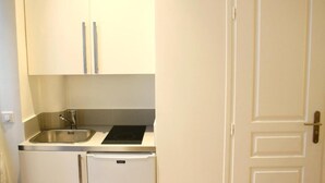Uma cozinha compacta com armários brancos, uma pia de aço inoxidável e um forno embutido.