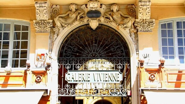 Uma entrada ornamentada com a placa “GALERIE VIVENNE” sobre um portão de ferro forjado.