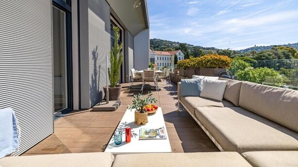 A modern outdoor living area with a sofa, dining table, and chairs, overlooking a scenic hillside. - Le Boréal penthouse, terrasse et vue panoramique (Cannes)