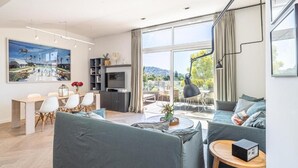 A modern living room with a dining area, a TV, and a large window with a view of the outdoors. - Le Boréal penthouse, terrasse et vue panoramique (Cannes)