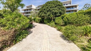 A pathway leading to a modern building with multiple balconies, surrounded by lush greenery. - Le Boréal penthouse, terrasse et vue panoramique (Cannes)