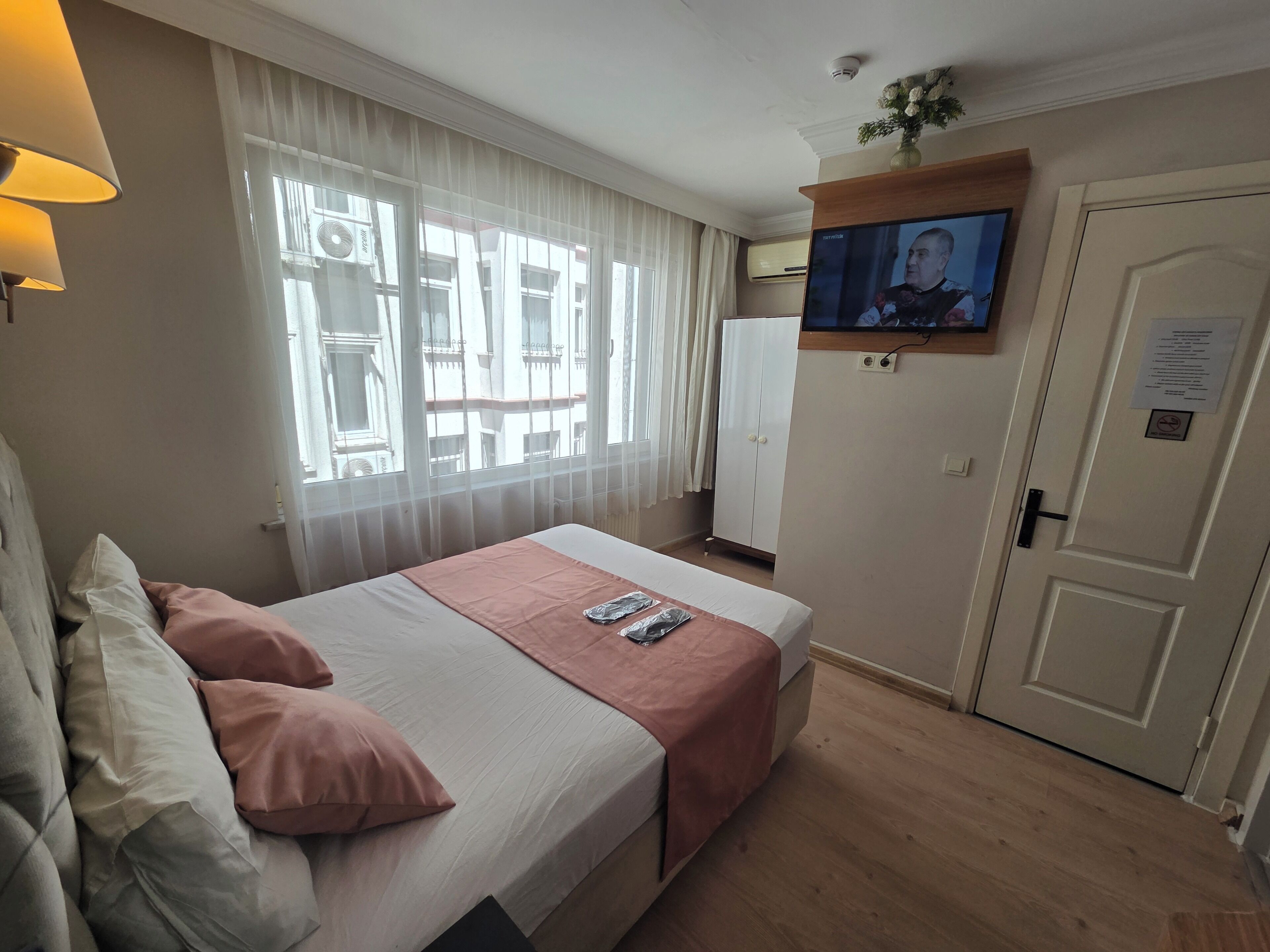 A hotel room with a bed, a television mounted on the wall, a wardrobe, and a door with a sign.