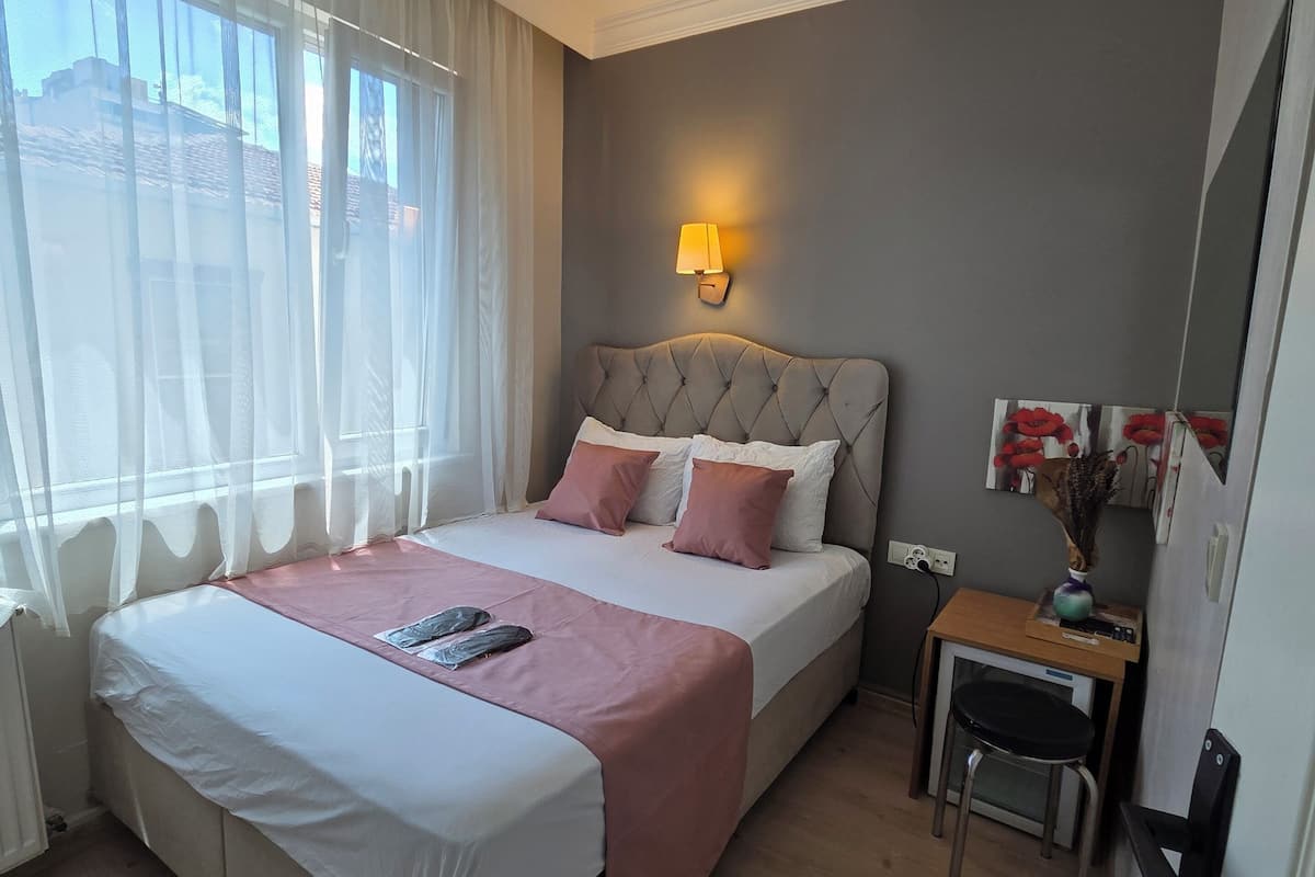 A hotel room with a large bed, a desk, a chair, and a window with curtains.