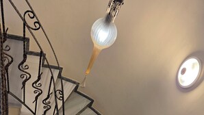Una escalera de caracol con barandilla de metal, un candelabro colgante y un extintor en la plataforma.