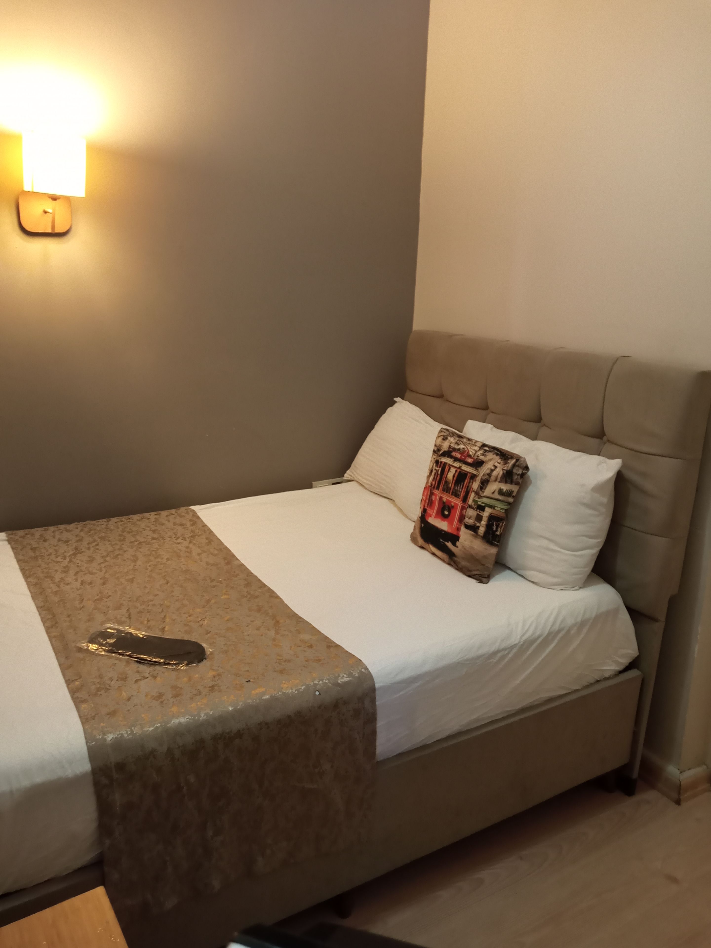 A single bed with a headboard, a bedside table, and a wall-mounted light fixture.