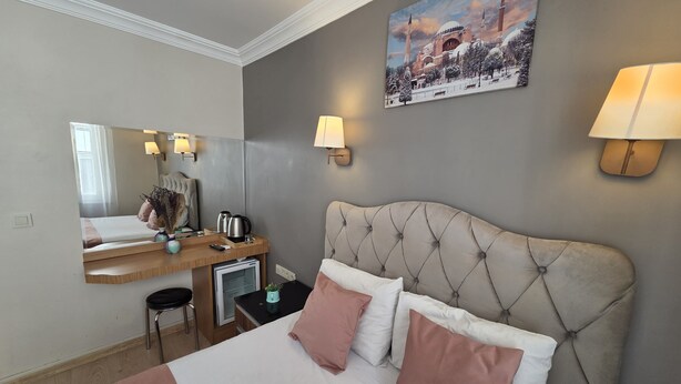 Una habitación de hotel con una cama, mesita de noche, lámpara y un cuadro de una mezquita.