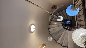 Una escalera de caracol con una araña y un aplique en la pared.