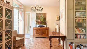 A well-lit hallway with a wooden cabinet, wicker chair, and a dining table. - L'Oranger maison pittoresque (Cannes)