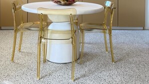 A modern kitchen with a round dining table, gold chairs, and a unique pendant light.