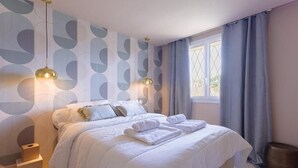 A modern bedroom with a bed, two bedside lamps, a window with curtains, and a wall with a geometric pattern.