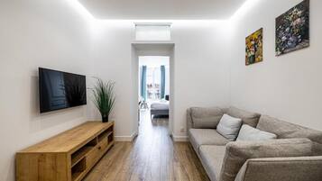 A modern living room with a wooden TV stand, a grey sofa, and two paintings on the wall.