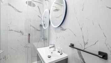 Un bagno moderno con parete in marmo, cabina doccia in vetro, lavandino bianco con specchio e maniglia di sostegno.