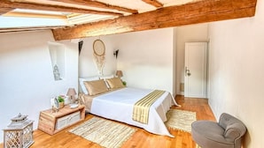 Une chambre avec un plafond en bois, un lit avec une literie blanche, une table de chevet avec une lampe et une chaise.