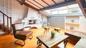 Un loft spacieux avec de hauts plafonds, des poutres apparentes, un coin repas avec une table et des chaises, une cuisine équipée de meubles et un escalier menant à un niveau supérieur.