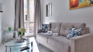 A modern living room with a beige sofa, a glass coffee table, and a painting on the wall.
