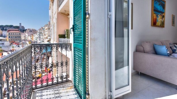 A balcony with a green shutter, a sofa with cushions, and a painting on the wall.