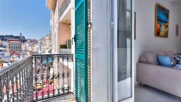 Un balcone con ringhiera metallica, una porta color petrolio e un divano con cuscini.
