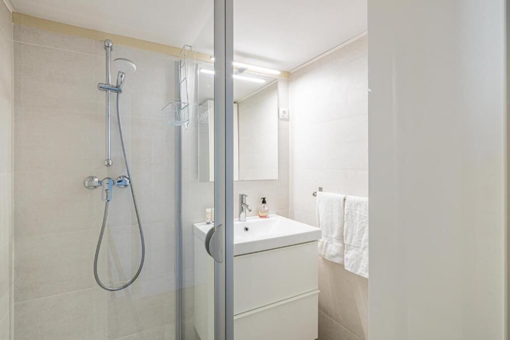 A modern bathroom with a glass-enclosed shower, a white sink, and a mirror.