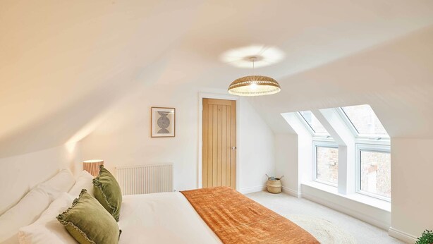 Et soveværelse med en stor seng, en hængende lampe, et vindue og en dør.