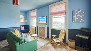 Ein Zimmer mit einem grünen Sofa, Holzstühlen, einem Kamin und Kunstwerken an den Wänden.
