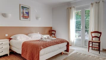 A bedroom with a bed, a nightstand, a chair, a window with curtains, and a wall-mounted light fixture.