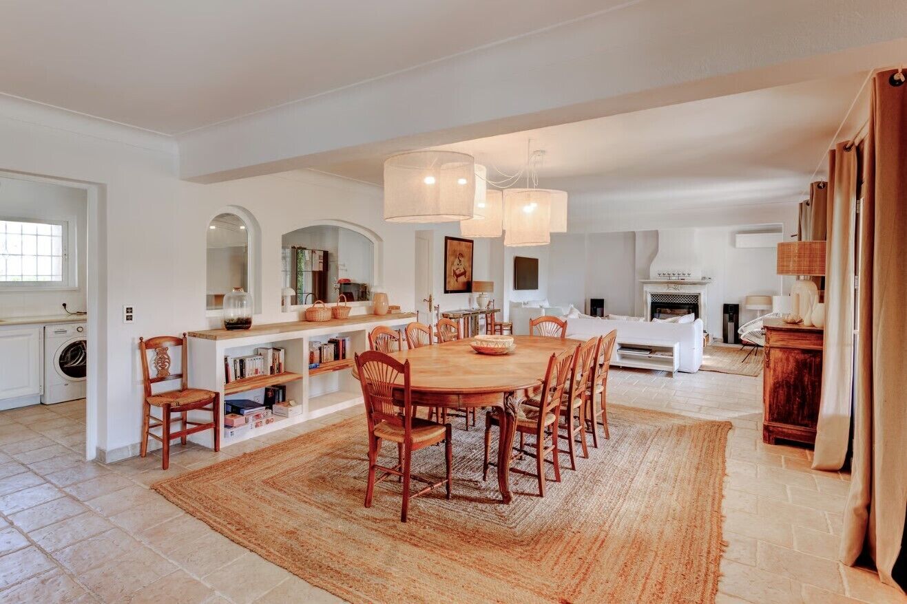 A spacious dining area with a large wooden table and chairs, surrounded by a woven rug.