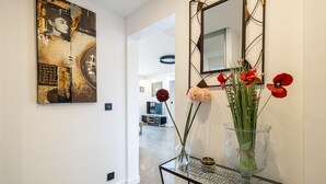 A hallway with a modern art piece, a glass vase with flowers, and a mirror on the wall.