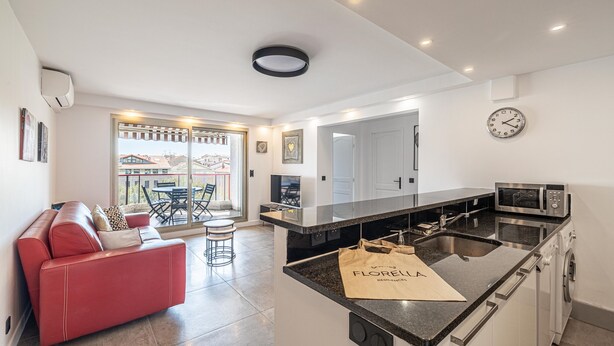 A modern kitchen with a central island, a red sofa, and a dining area with a view.