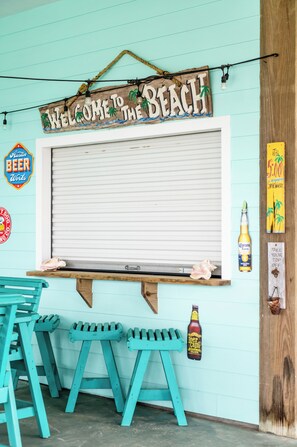 Eine Bar im Strandstil mit einem 'Welcome to the Beach'-Schild, einem Zapfhahn und einer hölzernen Bank.