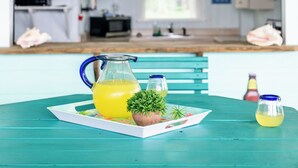 Ett kök med en tv, en skylt med texten ”Välkommen till stranden” och ett bord med en kanna gul dryck och en liten växt.