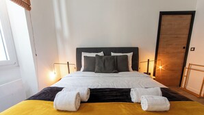 Una cama bien hecha con ropa blanca, cabecera negra y dos lámparas de noche.