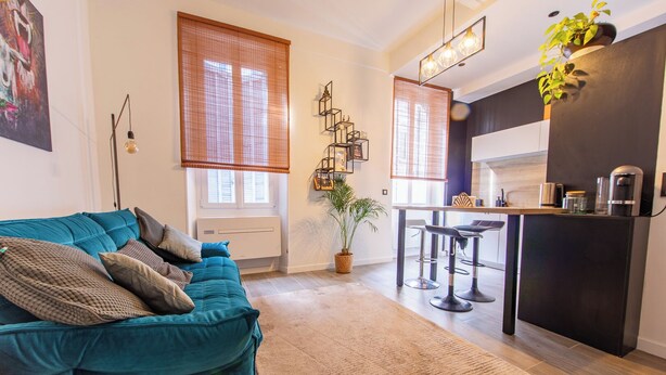 Una sala de estar moderna con un sofá color turquesa, una zona de cocina con un refrigerador negro y un comedor con taburetes de bar.