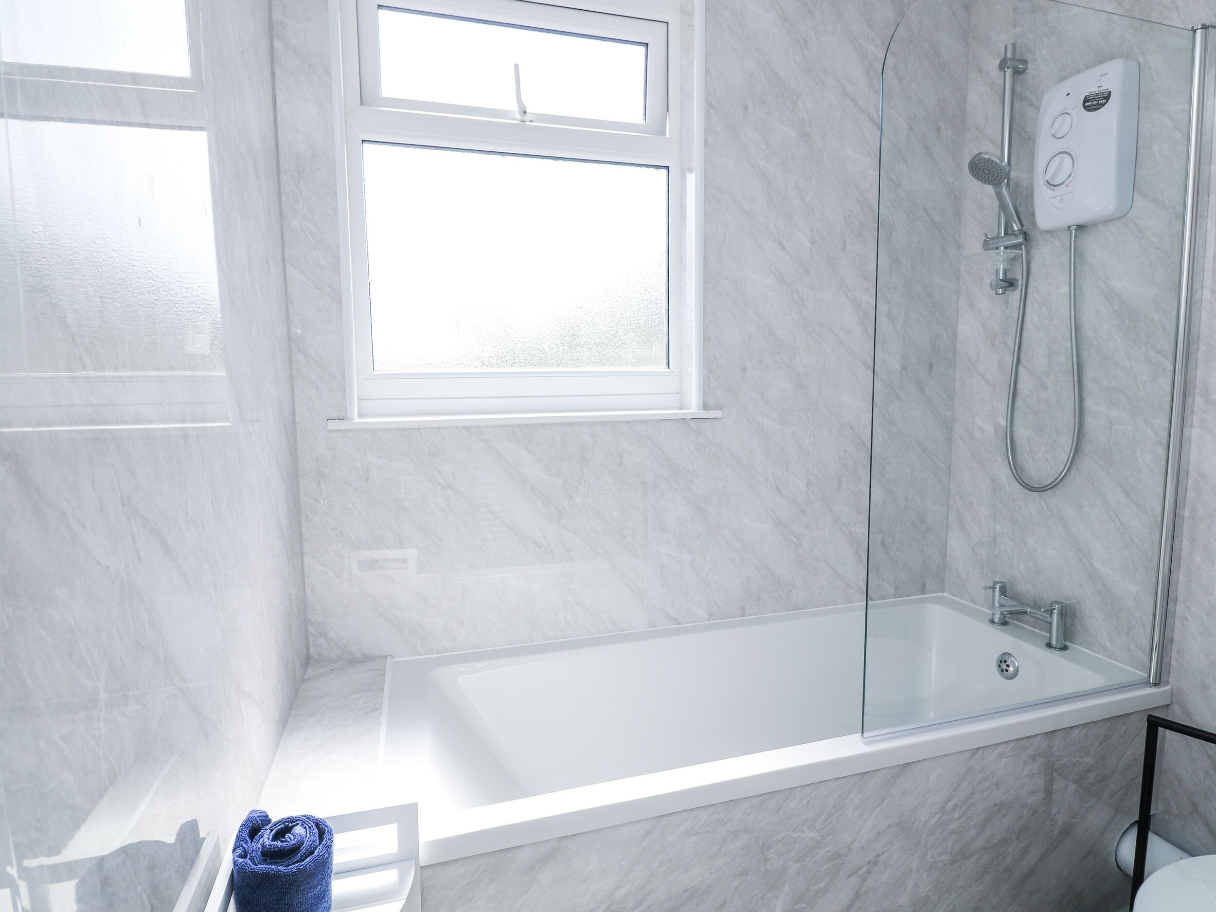 A modern bathroom with a bathtub, shower, and a window providing natural light.