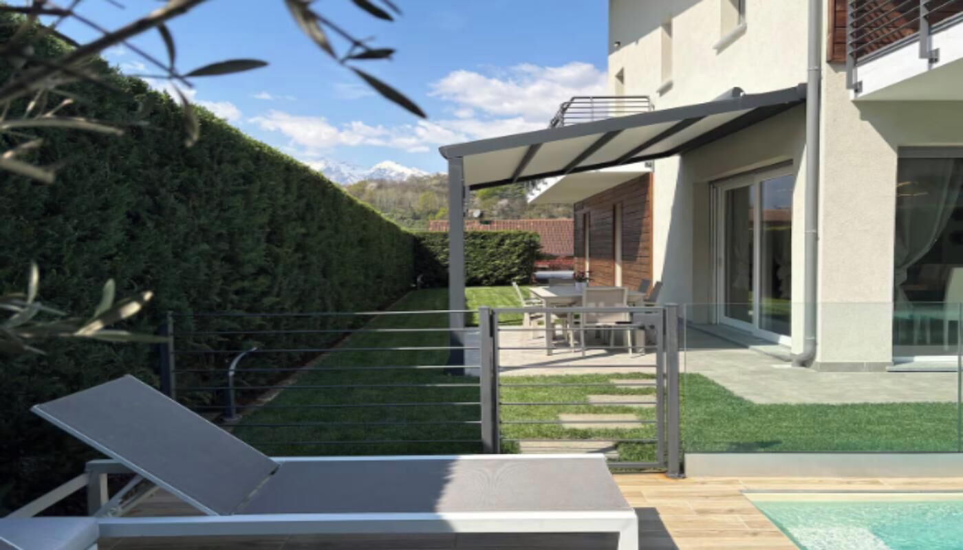 Een modern terras buiten met een zwembad, een ligstoel en een overdekte zithoek.