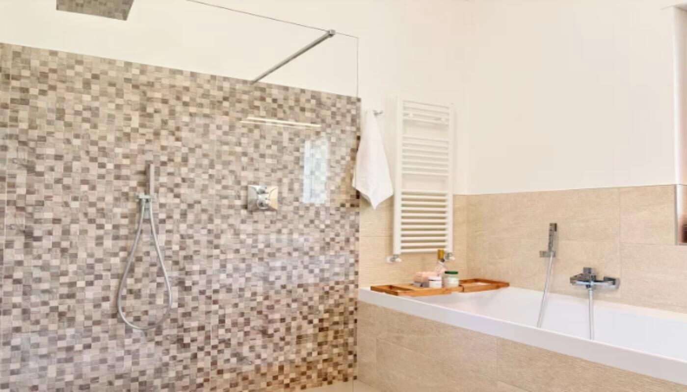 Een moderne badkamer met een douche, een badkuip en een betegelde wand.