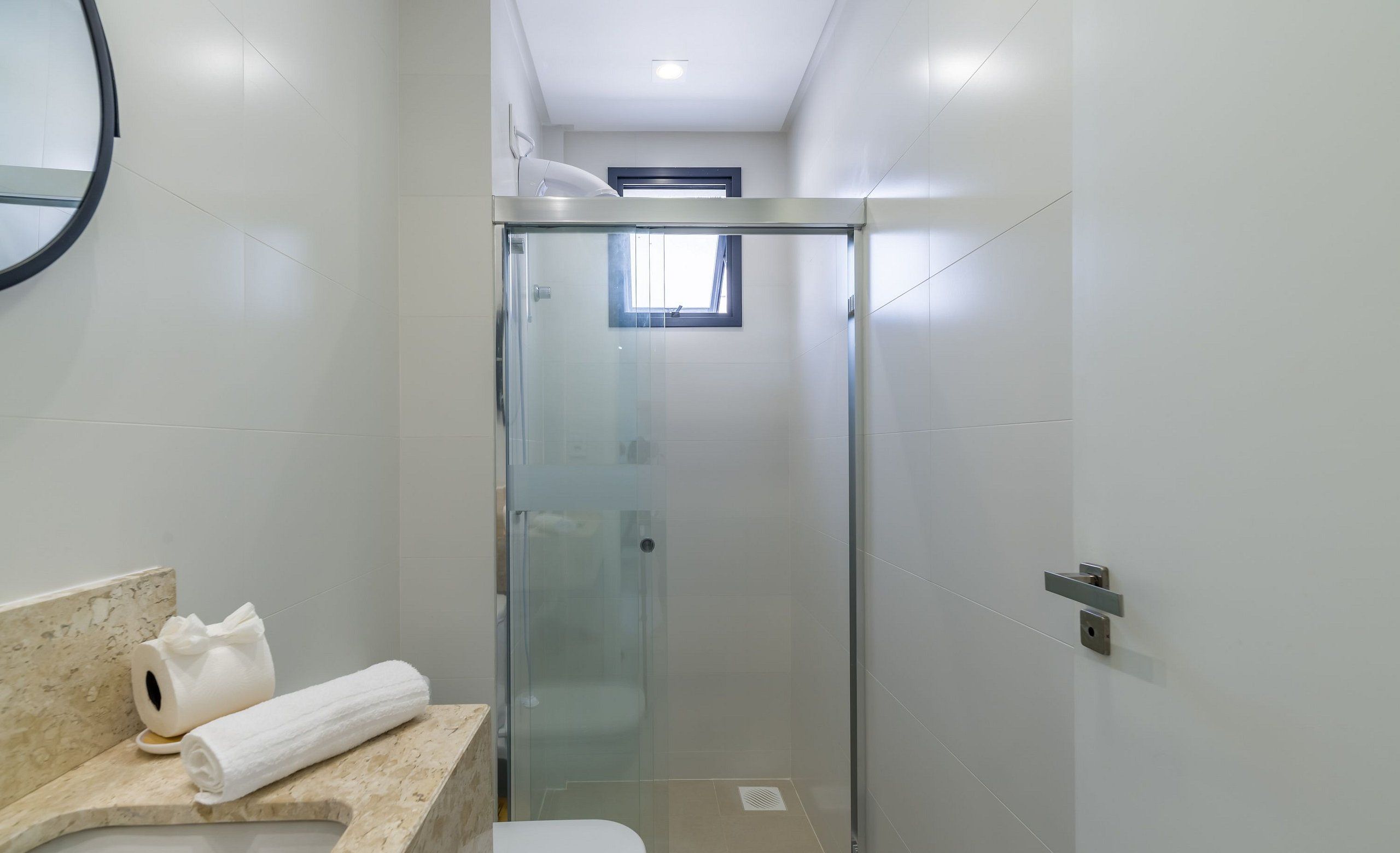 A modern bathroom with a glass-enclosed shower, a toilet, and a sink with a marble countertop.