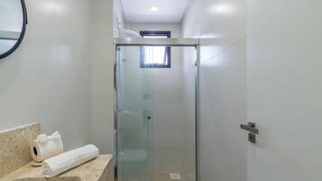A modern bathroom with a glass-enclosed shower, a toilet, and a sink with a marble countertop.