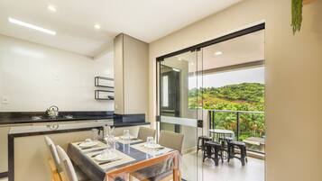 Cozinha moderna com área de refeições, varanda com vista para o verde e porta de vidro deslizante.