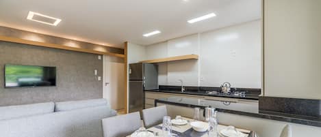 A modern kitchen with a dining area, a sofa, and a flat-screen TV.