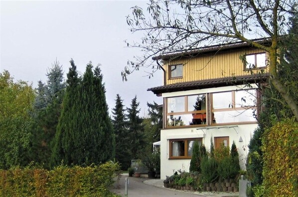 A two-story building with a balcony, surrounded by trees and shrubs.
