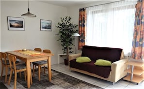 Een woonkamer met een bank, een eettafel, stoelen, een plant en een lamp.