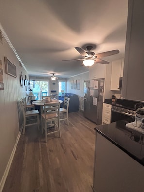 A kitchen with a dining area, wooden flooring, ceiling fans, and a refrigerator. - 'Just Chillaxin'-2-bedroom condo in lovely Ocean Isle Beach, NC-oceanview & pool (Ocean Isle Beach)