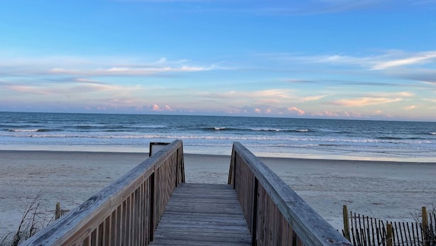 A wooden boardwalk leading to a beach with a clear view of the ocean.