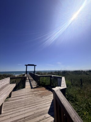 A wooden boardwalk leading to a viewpoint with a clear view of the ocean and distant land.
