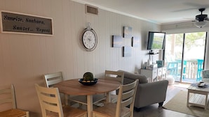 A dining area with a round table, four chairs, a clock, and a sign on the wall.
