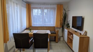 Un espace repas comprenant une table, des chaises, un banc, une plante en pot, un téléviseur et un meuble.