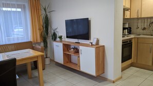 Un espace de vie compact comprenant un coin cuisine, un coin repas et un téléviseur fixé à un meuble.