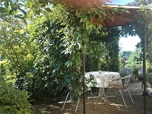 Une terrasse extérieure avec une table et des chaises, entourée d’une végétation luxuriante.