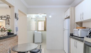 A compact kitchen with a refrigerator, microwave, and oven. There's a small dining table and chairs. A potted plant is on the counter. - 2BR Full apt Beachfront Ese0102 (Balneário Camboriú)